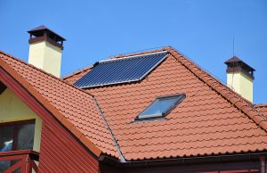 Energy efficiency concept. Closeup of solar water panel heating on red tiled house roof with lightning protection and chimney.